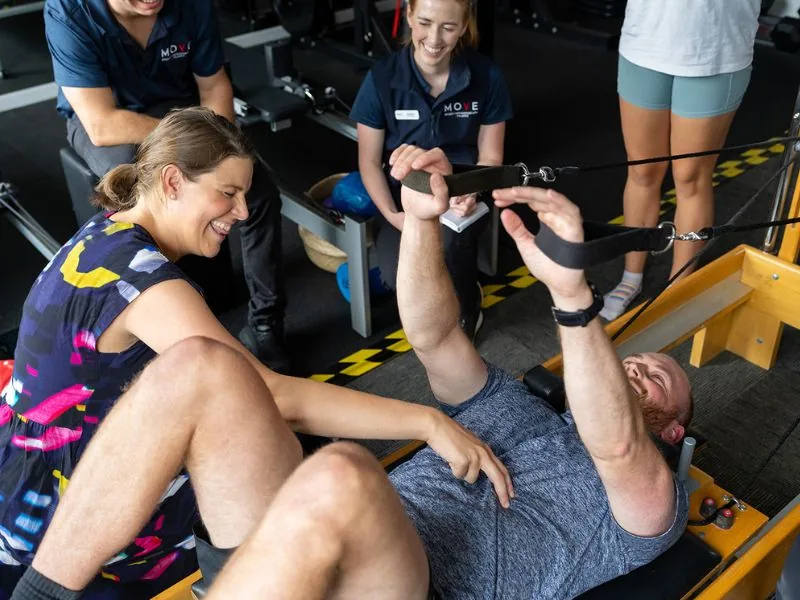 Clinicians laughing together while practising arm spring exercises on a reformer during a clinical Pilates course