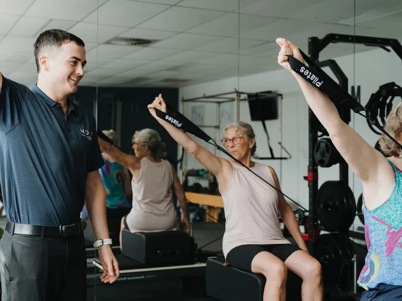 Clinician adjusting a client's leg position during a small group clinical Pilates class