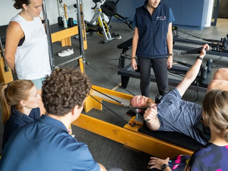 Clients performing standing exercises on reformers during a supervised group clinical Pilates class